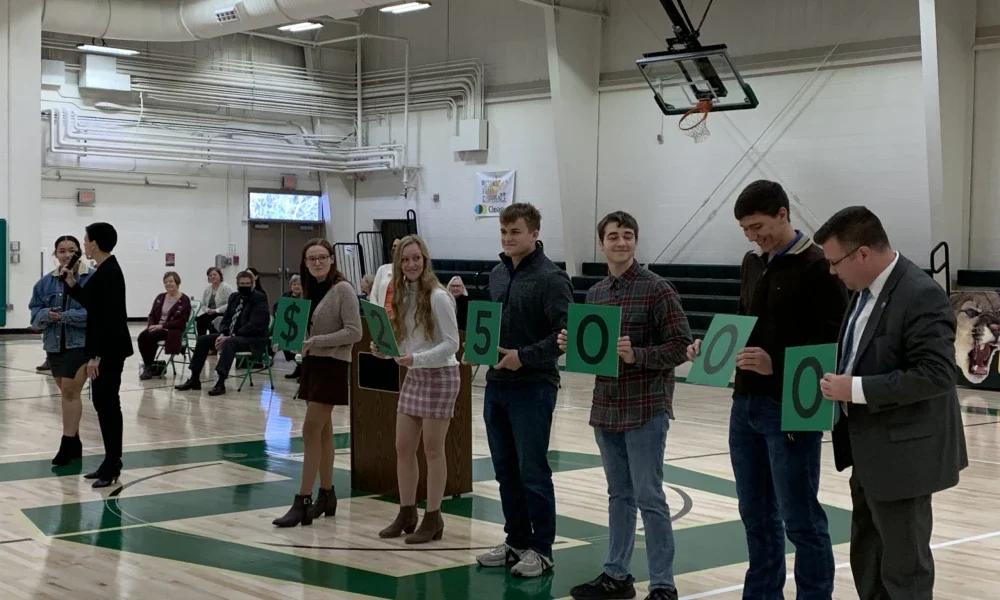 State Superintendent of Schools W. Clayton Burch joins East Hardy High School students as they hold cards designating the financial award Wolfe receives as part of the Milken program.