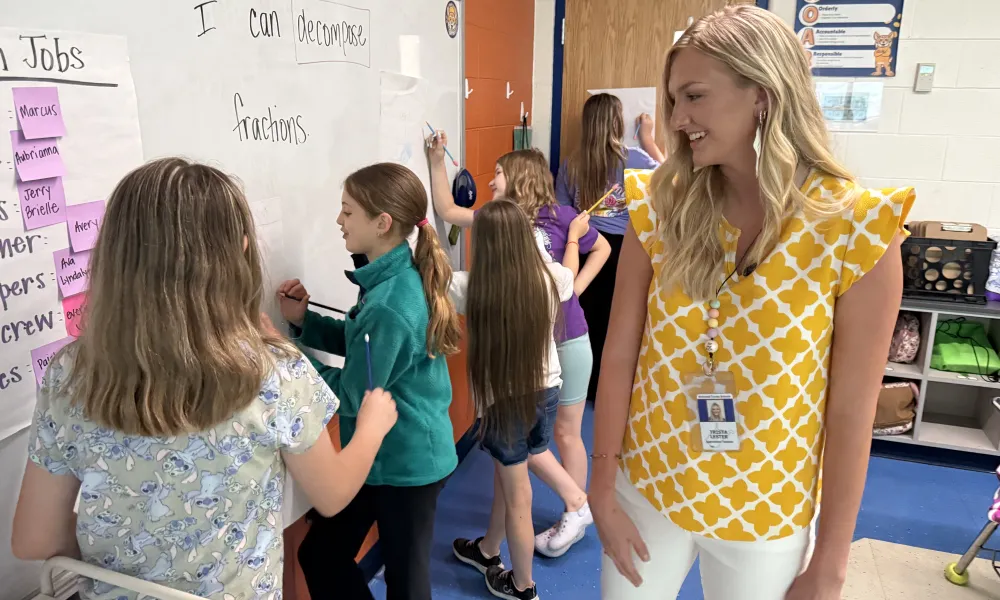 Female teacher smiling at students while they complete an activity.
