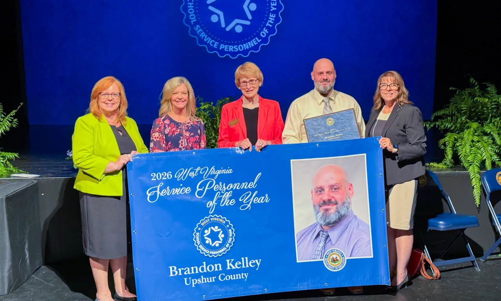 Five people holding a banner. 2026 School Service Personnel of the Year Brandon Kelley.