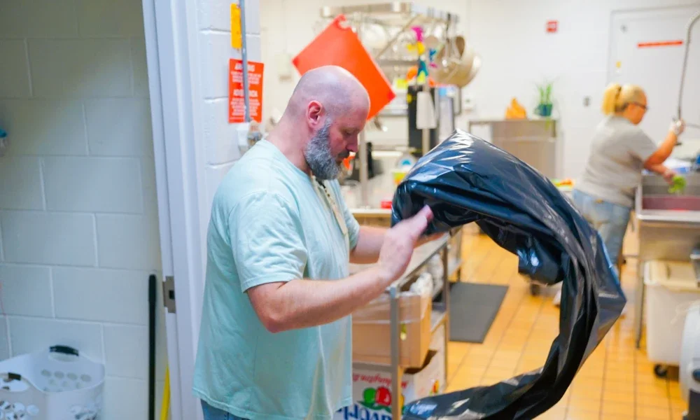 Brandon Kelley fluffing out a trash bag to place it in a trash can. 