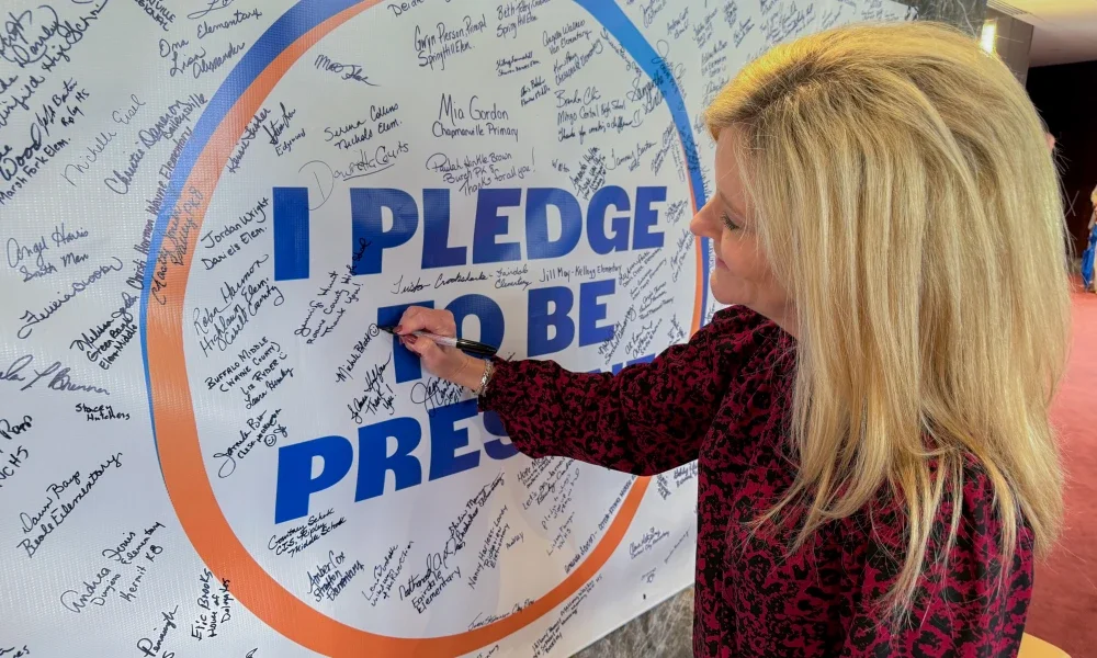 Michele Blatt signing a "I pledge to be present" banner.