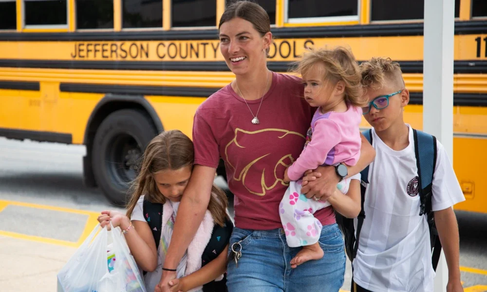 A family walking into school with a school bus behind them.