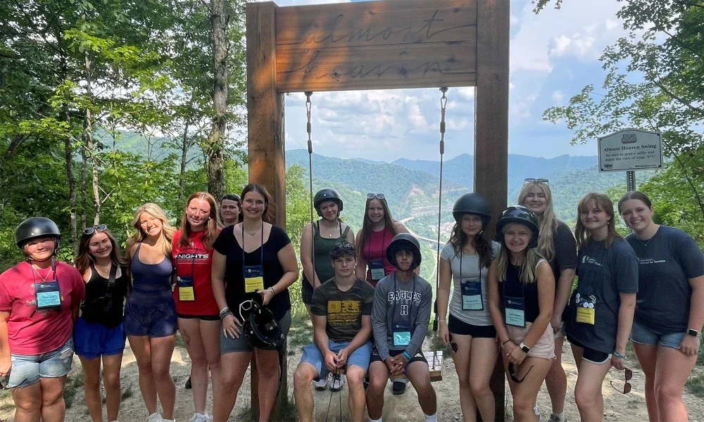 Students smiling and posing in front of a large wooden outdoor swing. 