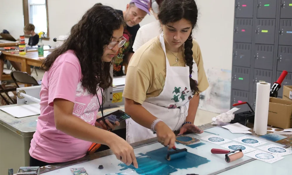 Two female students preparing ink for use in a printmaking exercise in a art room.