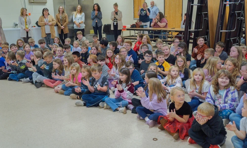 Students sitting on the floor clapping and smiling.