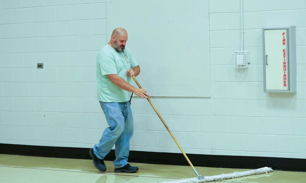Brandon Kelley holding a broom and sweeping the floor.