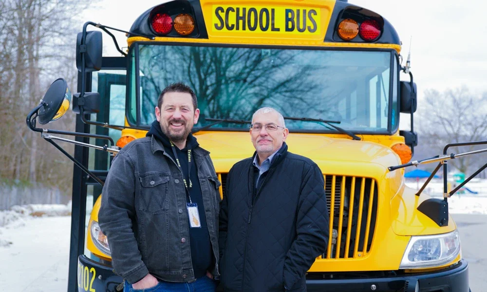 AJ Cline and Jimmy Lacy smiling while standing in front of a school bus.