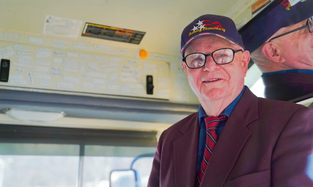 John Sitar smiling while standing beside the driver's seat on a school bus.