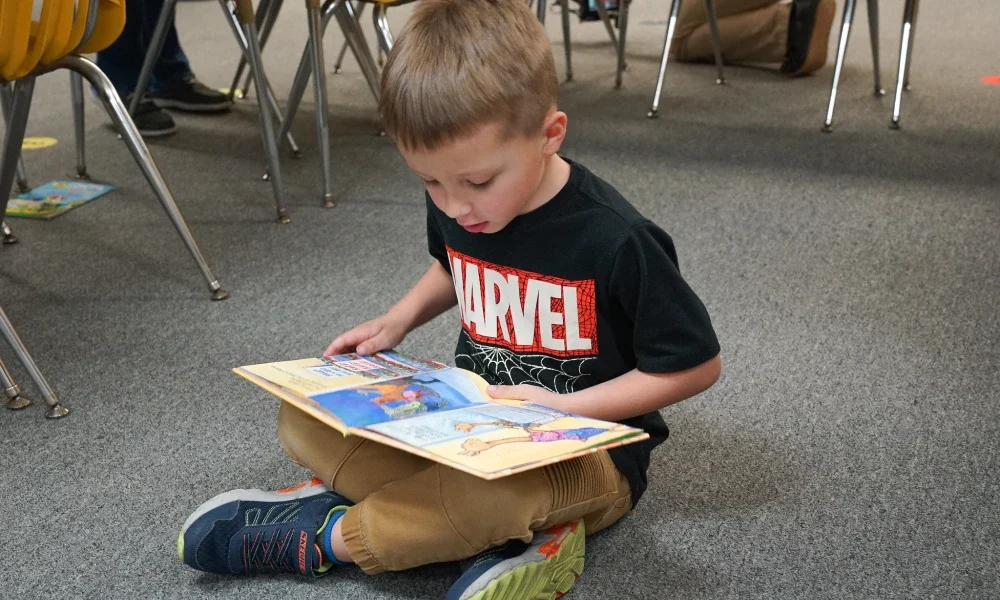 A child sitting on the floor while reading a book.