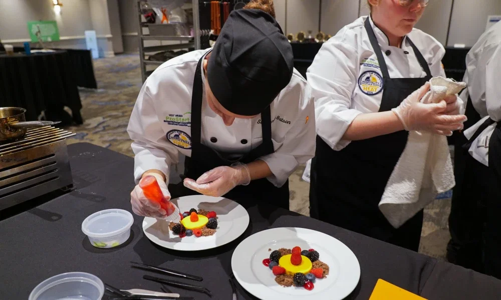 A person adding a fruit drizzle to a dessert plate.