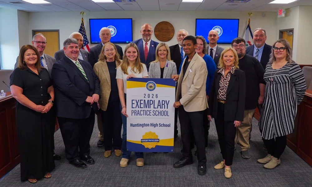 Members of Huntington High School and West Virginia Board of Education members smiling while holding an Exemplary Practice School banner.