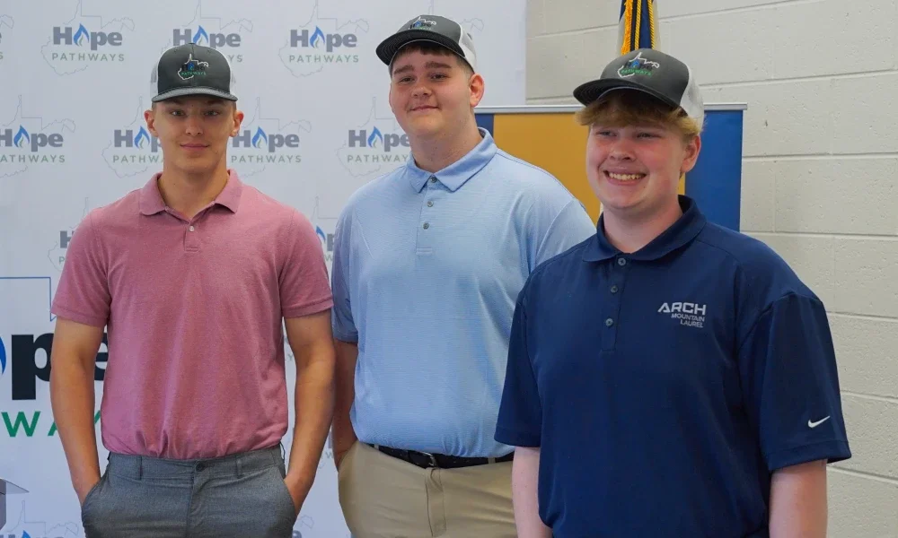 Three students smiling while wearing Hope Gas hats.