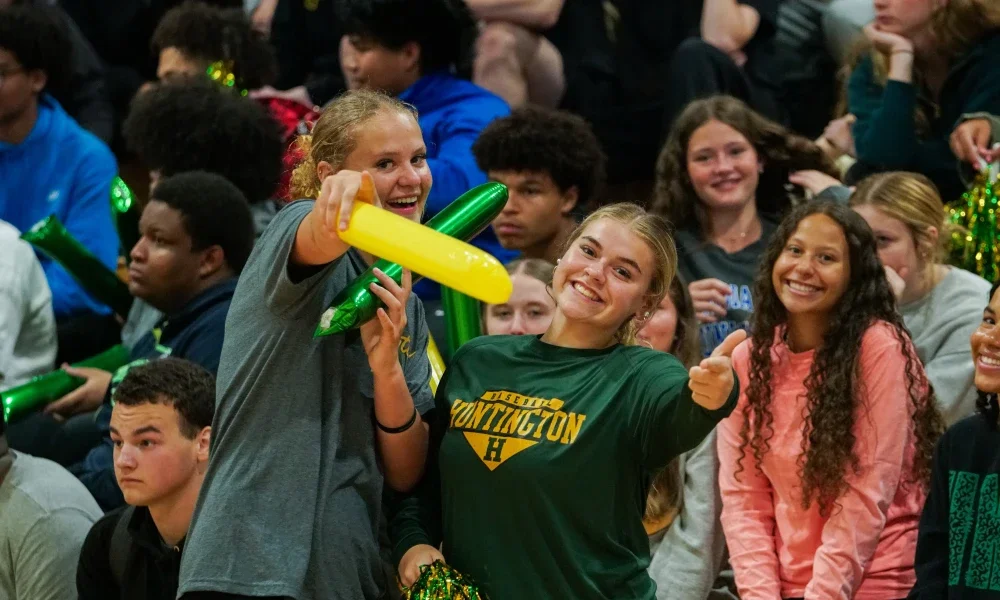 Two students smiling and pointing while other students smile behind them. 