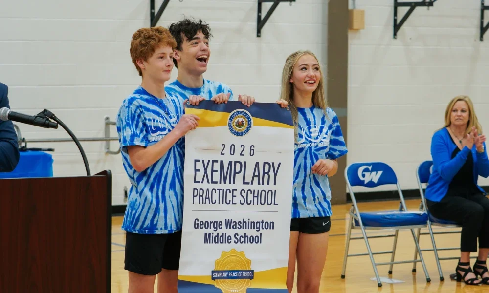 Students smiling while holding an Exemplary Practice School banner. 