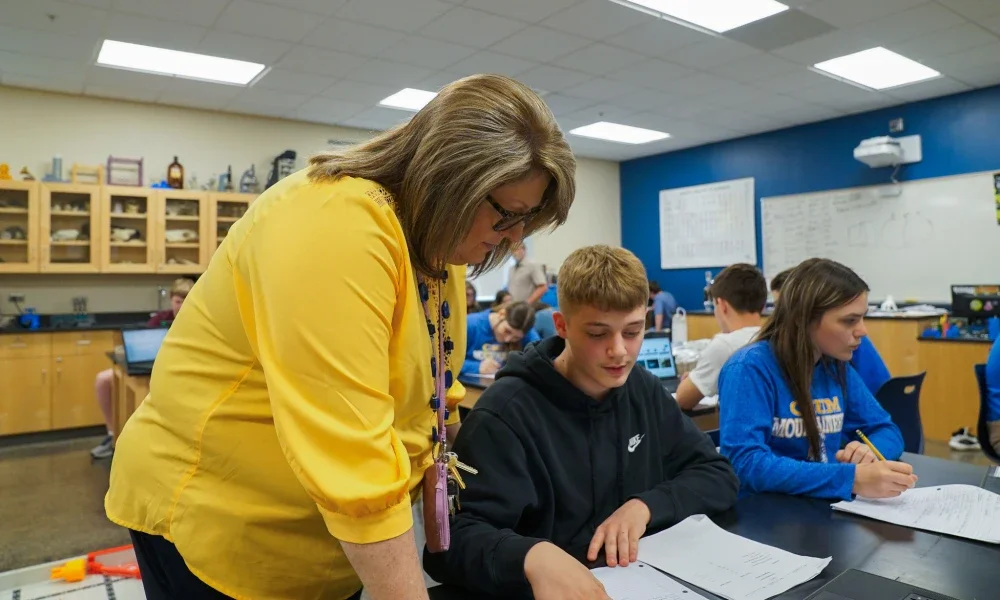 Female teacher assisting student in classroom.