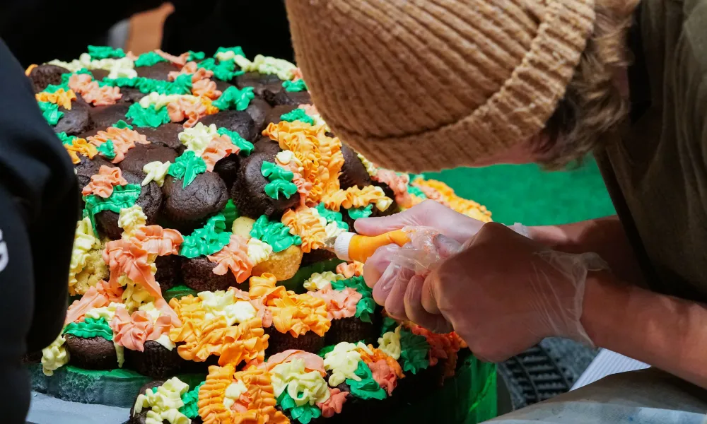 A student placing icing on a cupcake. 