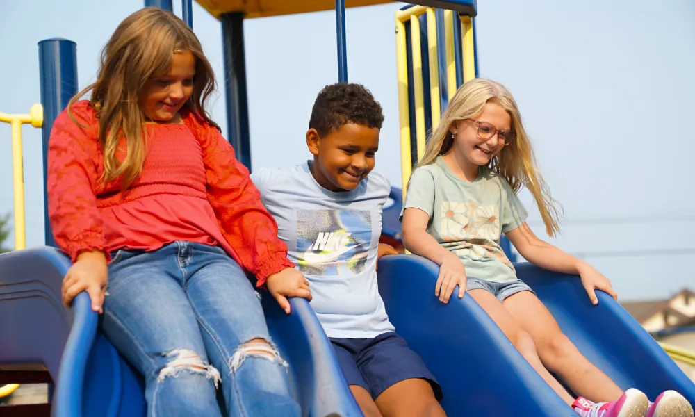 Three children smiling while sliding down a slide. 