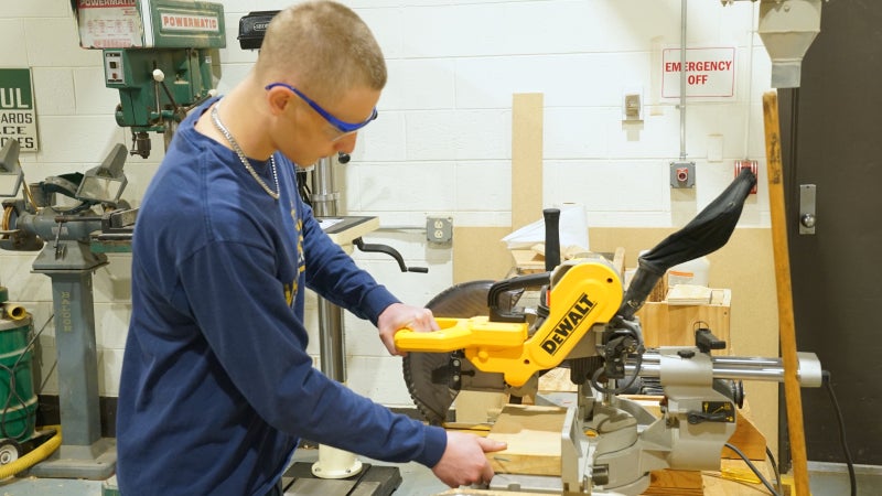 Person standing at a circular saw cutting wood.