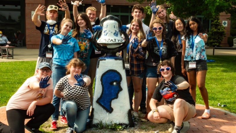 Students gathered together displaying blue painted hands that they are using to decorate a statue on WVU campus