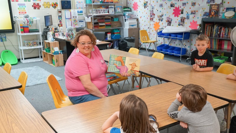 Person reading a book to students.