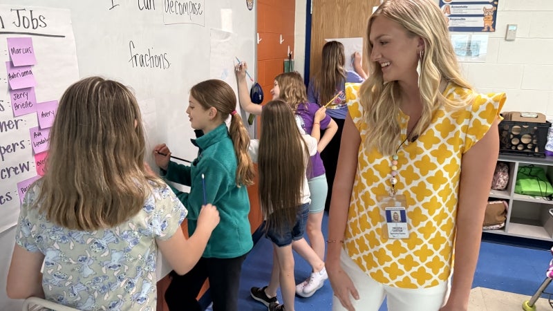 Female teacher smiling at students while they complete an activity.