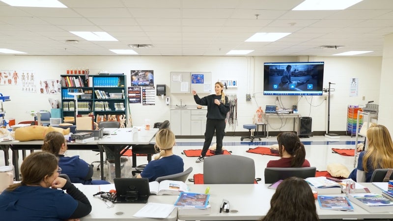 A woman teaching nursing students front the front of the classroom.