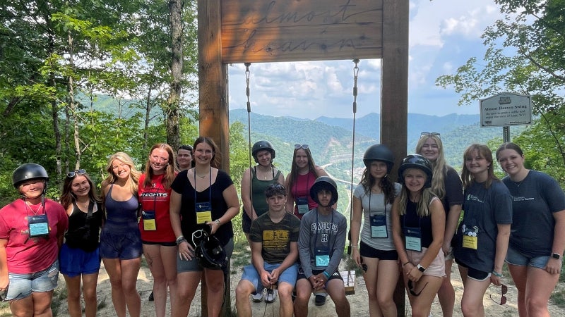Students smiling and posing in front of a large wooden outdoor swing. 