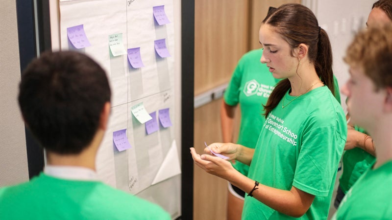 Students brainstorming ideas for a project by placing sticky notes on a chart.