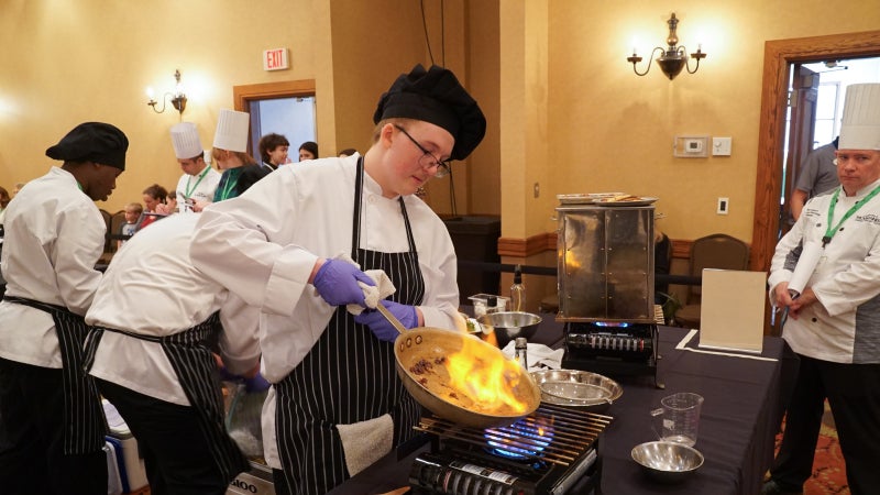 A student cooking something in a pan.