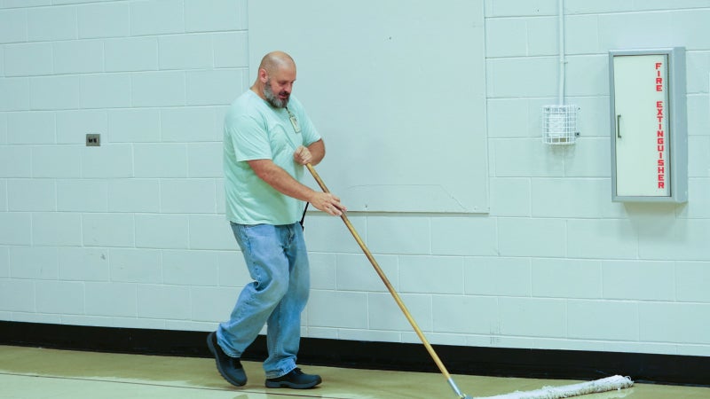 Brandon Kelley holding a broom and sweeping the floor.