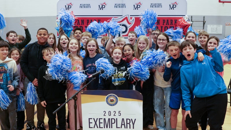 Students celebrating and smiling while standing behind a banner that says "Exemplary Practice School.