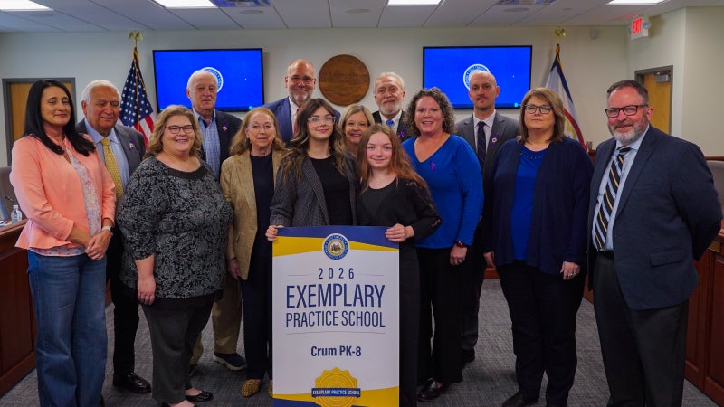 Members of Crum PK-8 and West Virginia Board of Education members smiling while holding an Exemplary Practice School banner.