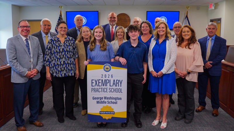 Members of George Washington Middle School and West Virginia Board of Education members smiling while holding an Exemplary Practice School banner.