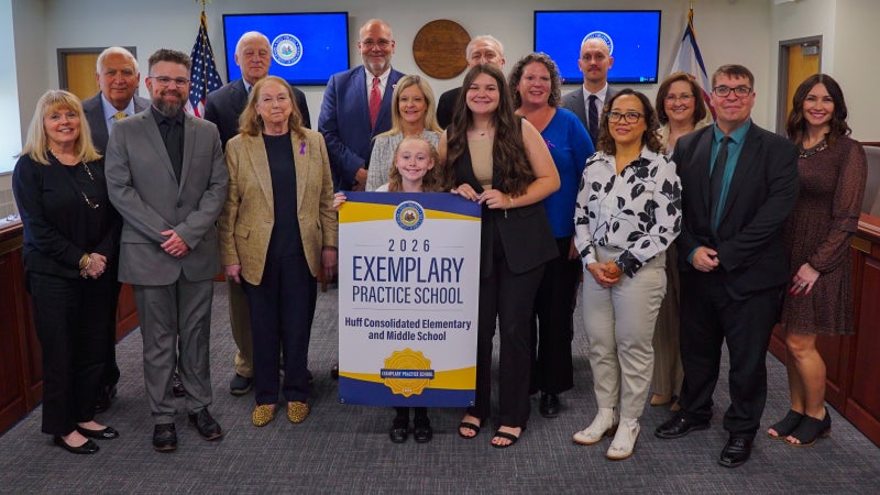 Members of Huff Consolidated Elementary and Middle School and West Virginia Board of Education members smiling while holding an Exemplary Practice School banner.
