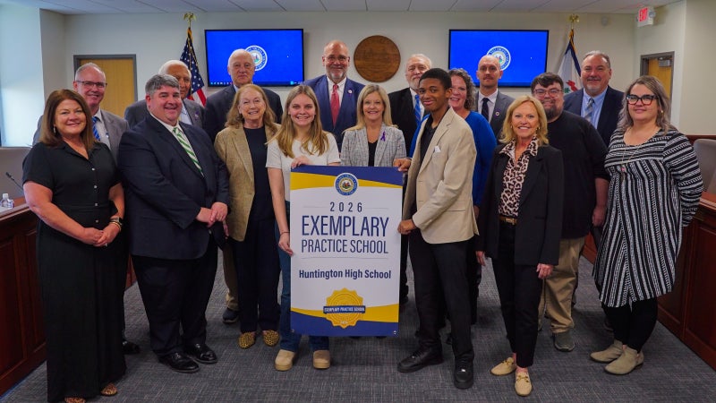 Members of Huntington High School and West Virginia Board of Education members smiling while holding an Exemplary Practice School banner.
