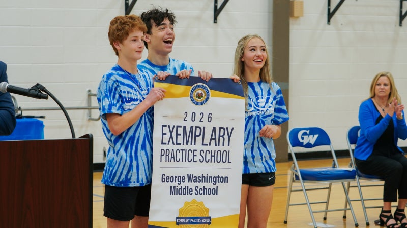 Students smiling while holding an Exemplary Practice School banner. 