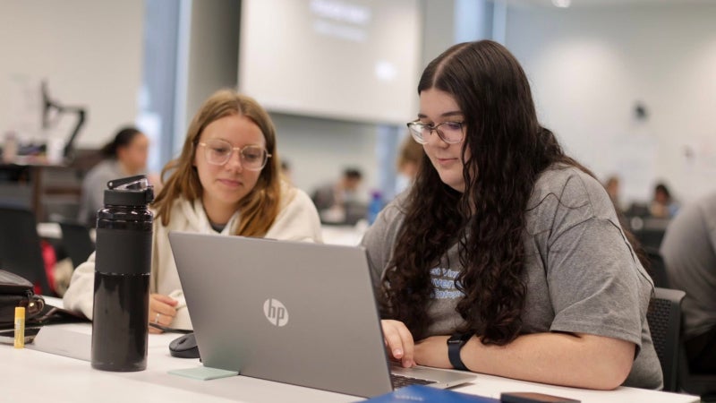 Two female students sitting looking at a computer. 