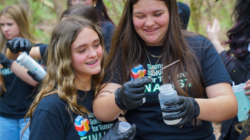 Two students smiling while holding a water sample. 