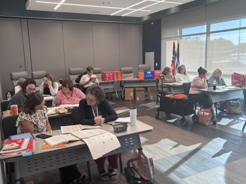 A group of people sitting at tables reading learning and training materials.