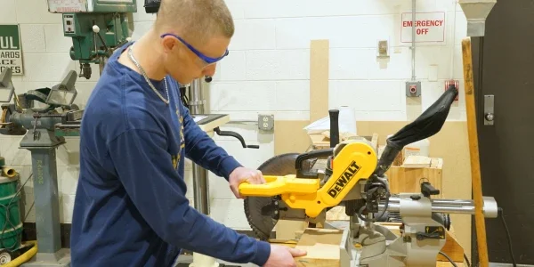Person standing at a circular saw cutting wood.