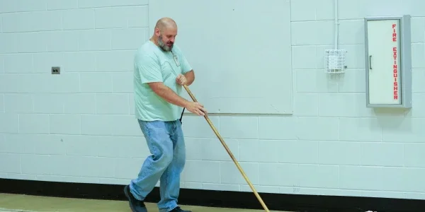 Brandon Kelley holding a broom and sweeping the floor.
