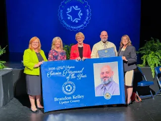 Five people holding a banner. 2026 School Service Personnel of the Year Brandon Kelley.