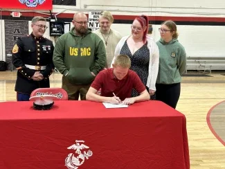 A person signing a document while other watch him sign it.