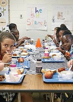 Kids sit at cafeteria table eating