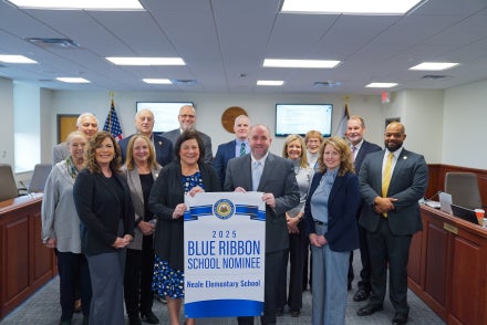 A group of people gathered around a banner with the words "2025 Blue Ribbon School Nominee Neale Elementary School" on it.