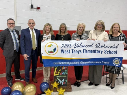 People holding a banner with the words "2025 Balanced Scorecard West Teays Elementary School exceeds standard in academic achievement and academic progress" on it.