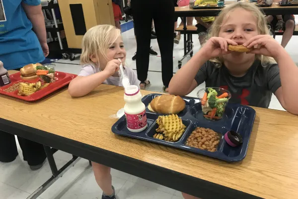 2 students sit a cafeteria table and eat
