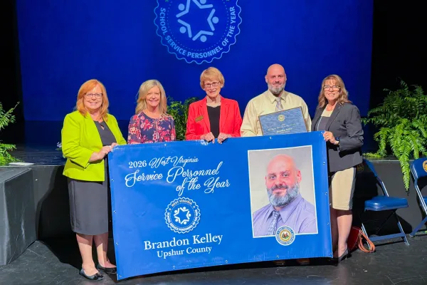 Five people holding a banner. 2026 School Service Personnel of the Year Brandon Kelley.