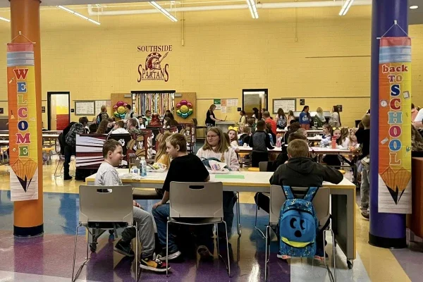 Students sitting at tables eating food inside of a school cafeteria.