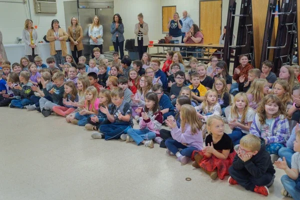 Students sitting on the floor clapping and smiling.